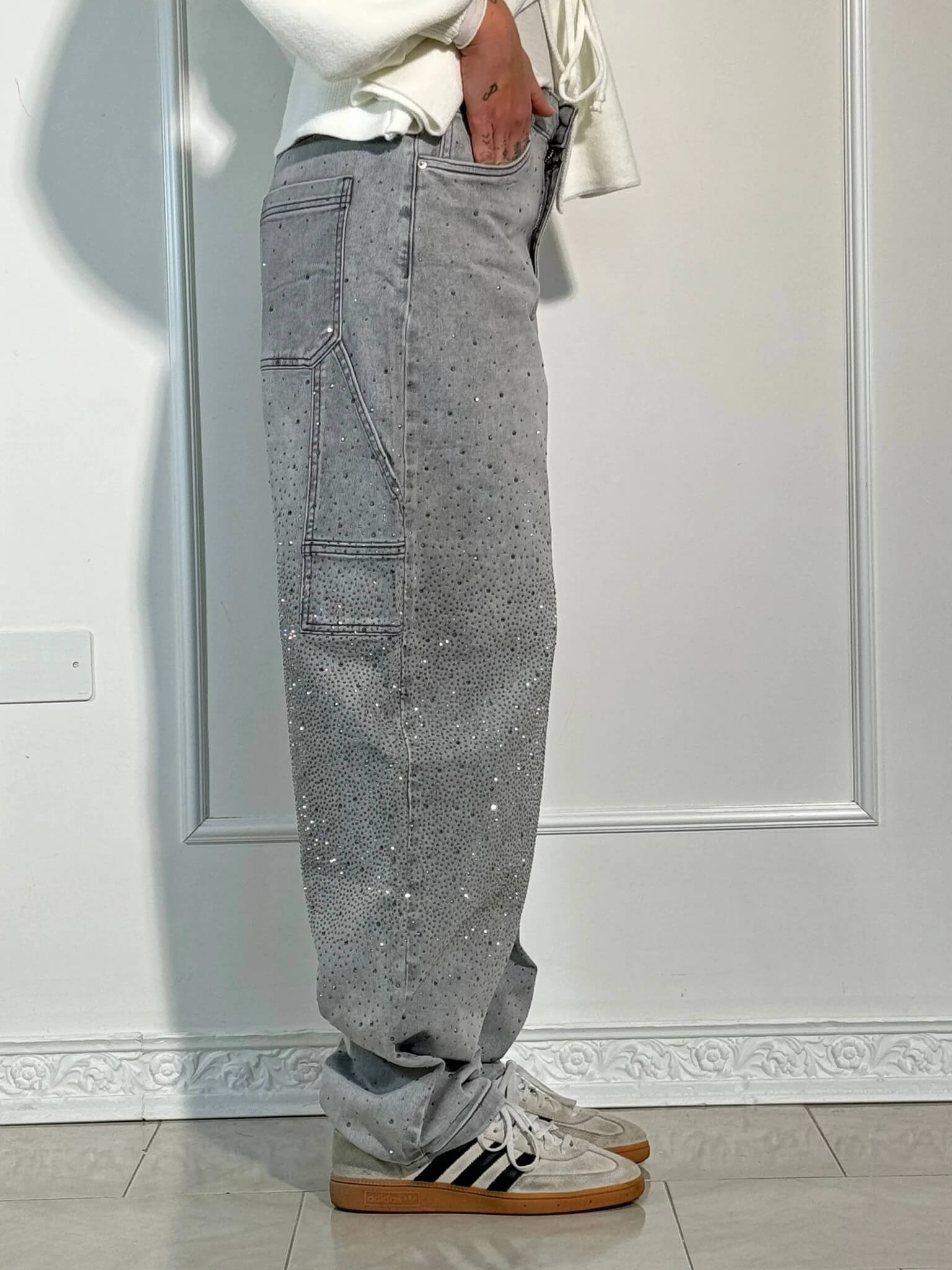 Jeans grigi con strass, tasche laterali, indossati con sneakers bianche e nere. Moda casual, abbigliamento uomo, stile urbano.