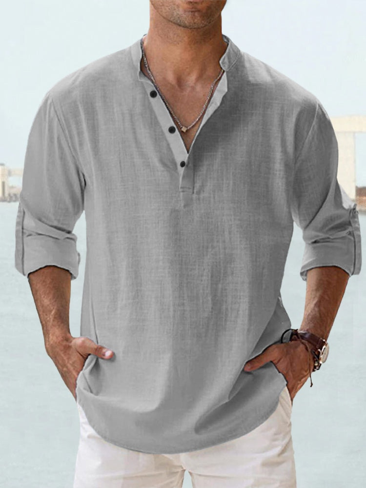 Camicia uomo lino grigia, maniche lunghe arrotolate, colletto alla coreana, abbottonatura parziale, stile casual estivo, sfondo marino.