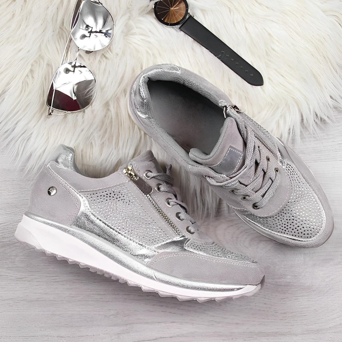 Scarpe da ginnastica grigie e argento su sfondo in legno chiaro, con occhiali da sole, orologio e tappeto bianco. Design moderno e casual.
