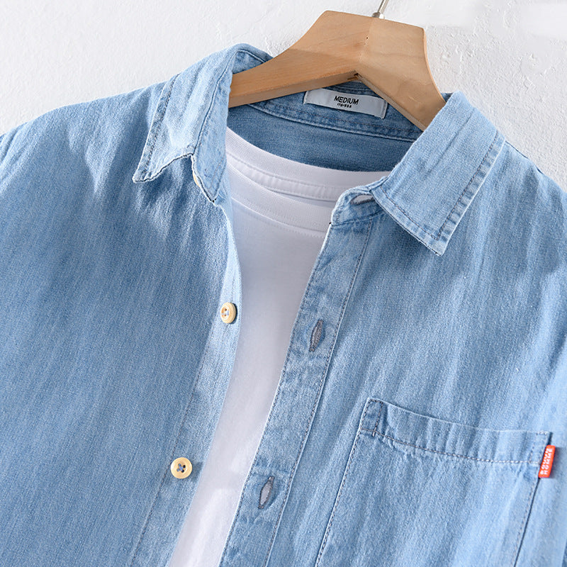 Camicia di jeans azzurra su gruccia, con taschino e bottoni in legno, sopra maglietta bianca. Moda casual uomo, abbigliamento denim.