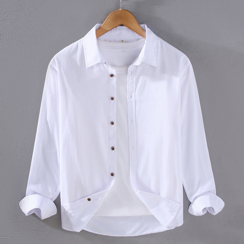 Camicia bianca da uomo in cotone, maniche lunghe, colletto classico, bottoni marroni, appesa su gruccia di legno, sfondo grigio.