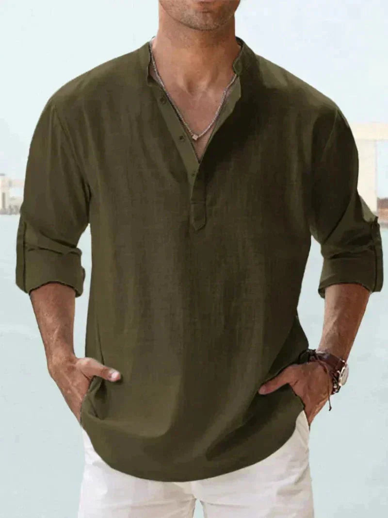Camicia uomo verde oliva, maniche lunghe arrotolate, scollo a V con bottoni, stile casual, indossata con pantaloni bianchi.