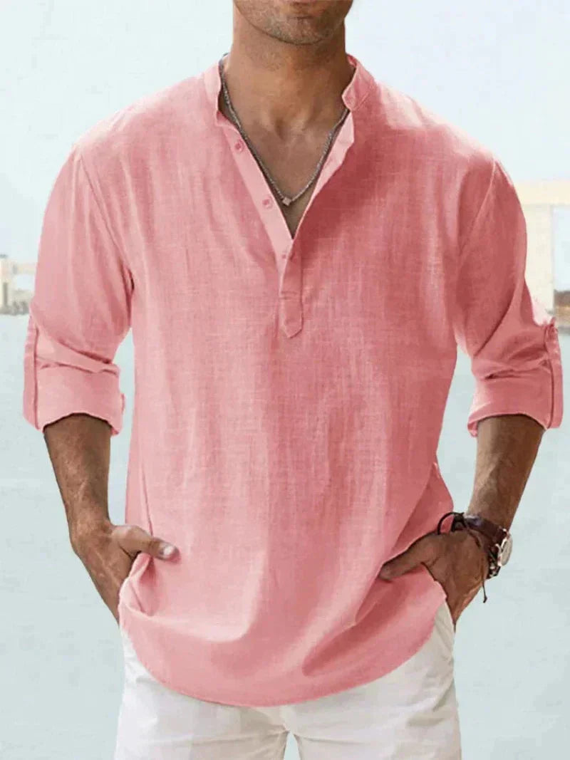 Camicia uomo in lino rosa, maniche lunghe arrotolate, stile casual estivo, scollo a V con bottoni, abbinata a pantaloni bianchi.