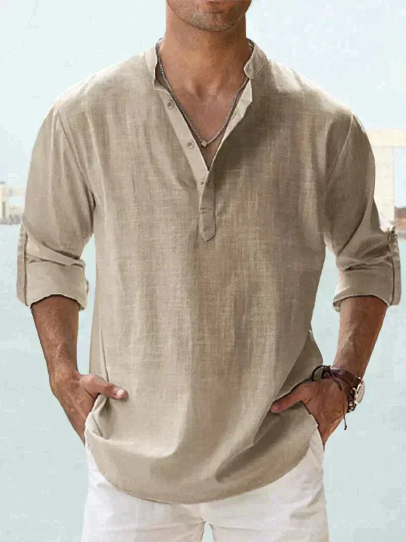 Uomo con camicia di lino beige a maniche lunghe, collo alla coreana, abbinata a pantaloni bianchi. Stile casual estivo maschile.
