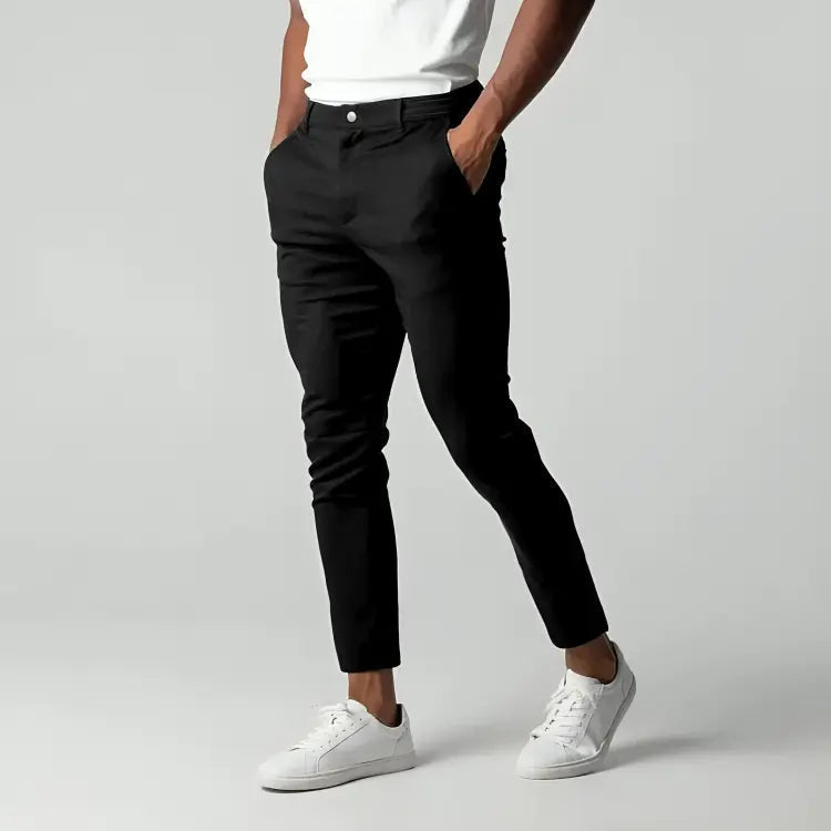 Pantaloni chino neri da uomo, vestibilità slim, abbinati a scarpe da ginnastica bianche e maglietta bianca. Moda casual elegante.