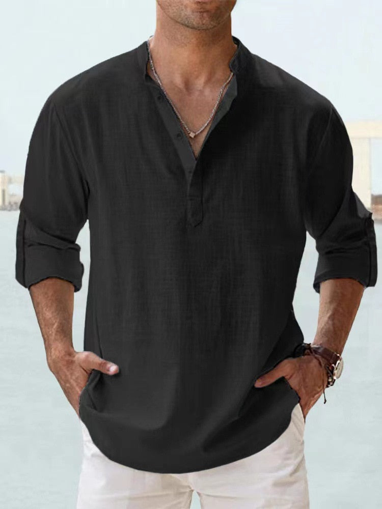 Camicia uomo nera in lino, maniche lunghe arrotolate, collo alla coreana, abbinata a pantaloni bianchi. Stile casual elegante.