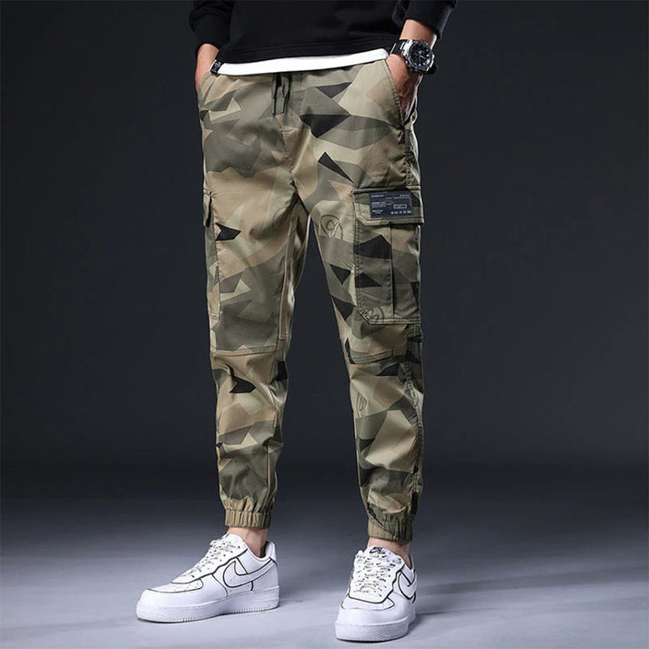 Pantaloni cargo mimetici da uomo, design moderno, tasche multiple, stile casual, abbinati a scarpe sportive bianche, moda streetwear.