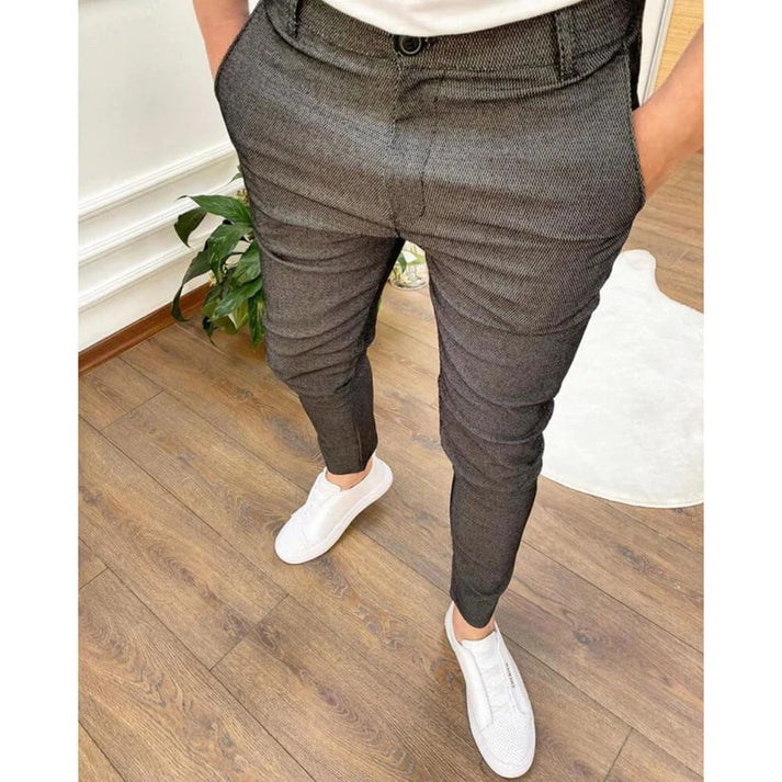 Pantaloni eleganti grigi da uomo, abbinati a scarpe da ginnastica bianche su pavimento in legno. Stile moderno e casual.