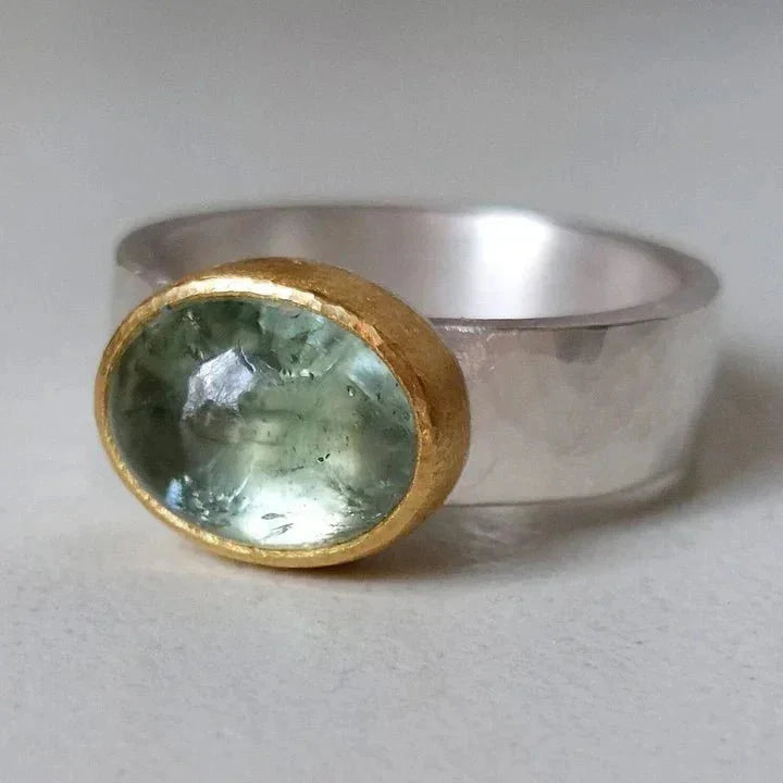 Silver-tone hammered ring with oval green stone in a gold bezel.